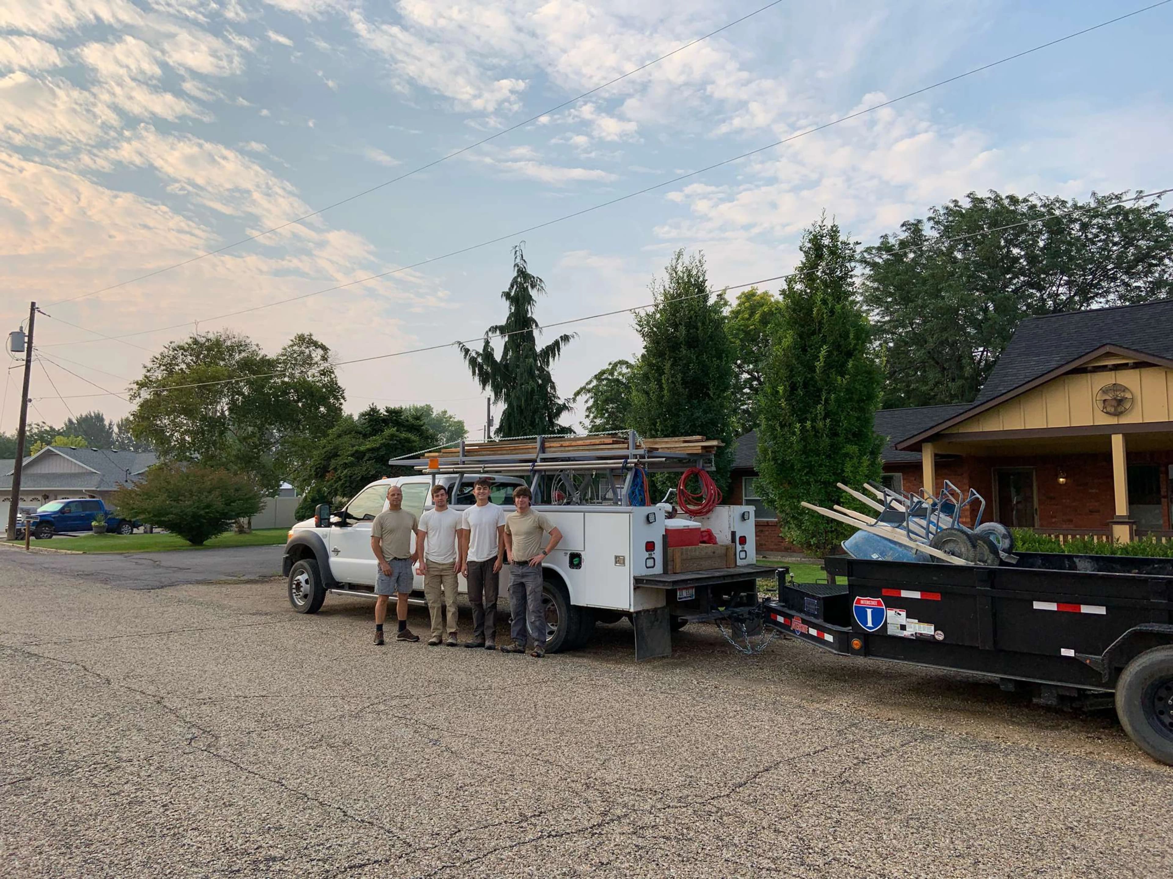 Four members of the crew standing in front of a work truck and equipment trailer at dawn