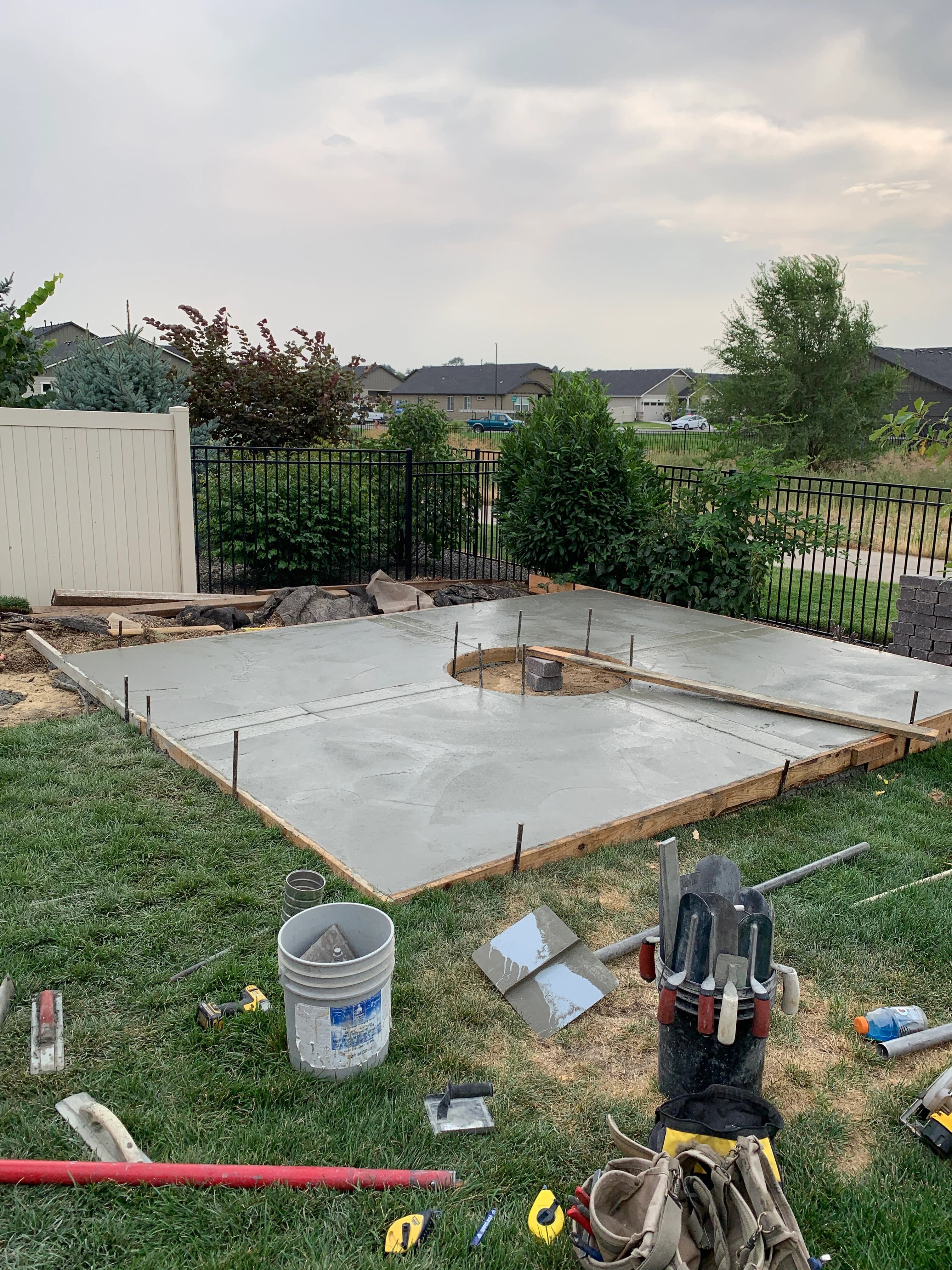 A freshly poured concrete patio still in its wooden forms, with tools scattered on the grass